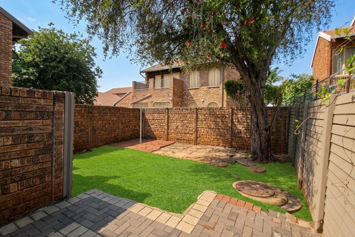 A private rear garden featuring a paved patio area, a well-maintained lawn, and brick boundary walls, providing a functional outdoor space.