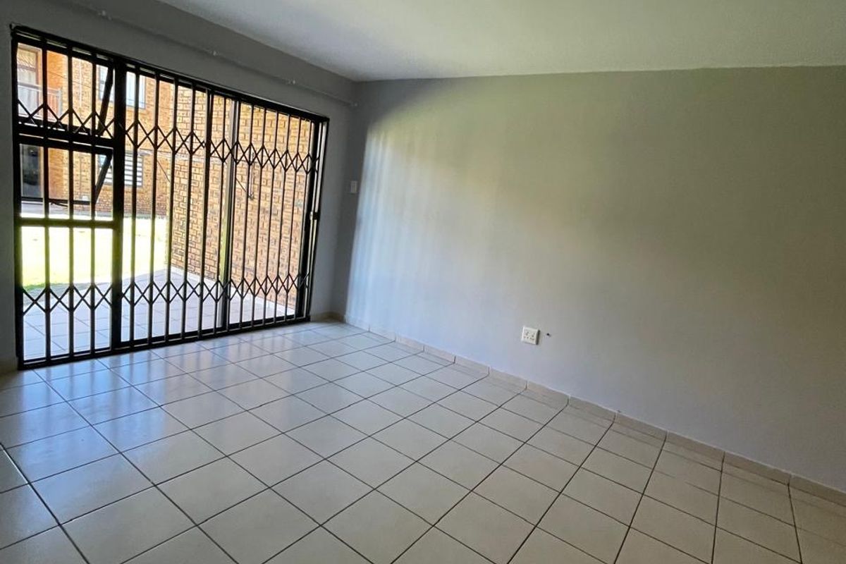An empty living room featuring neutral tiled flooring, a sliding door with a security gate, and access to an outdoor area.