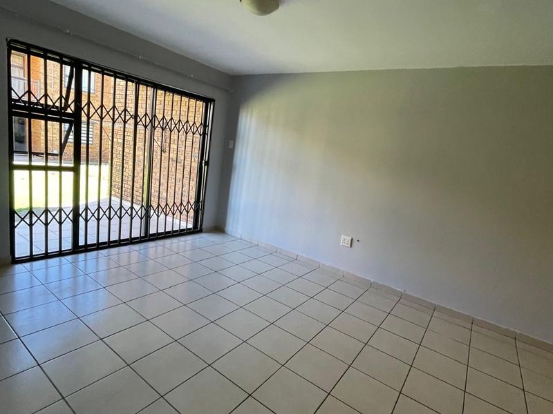 An empty living room featuring neutral tiled flooring, a sliding door with a security gate, and access to an outdoor area.