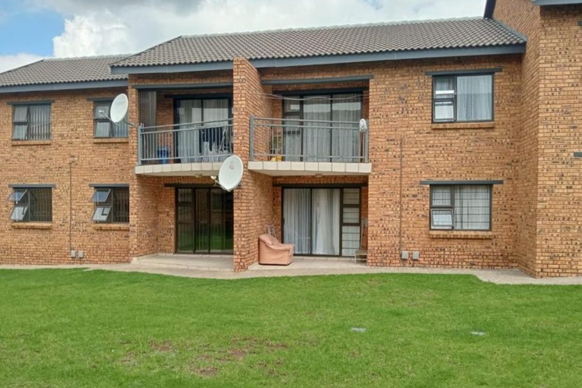 Rear view of a face brick apartment building featuring balconies, sliding glass doors, and security bars overlooking a communal lawn area.