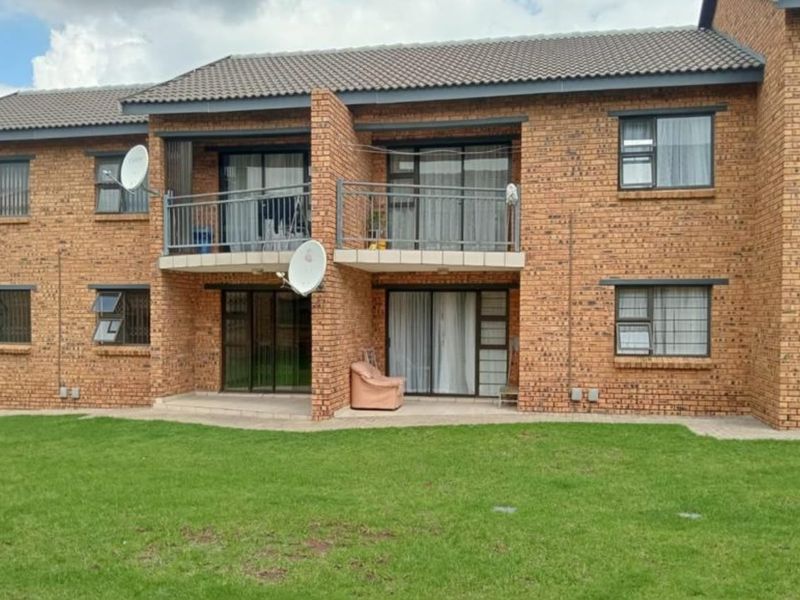 Rear view of a face brick apartment building featuring balconies, sliding glass doors, and security bars overlooking a communal lawn area.