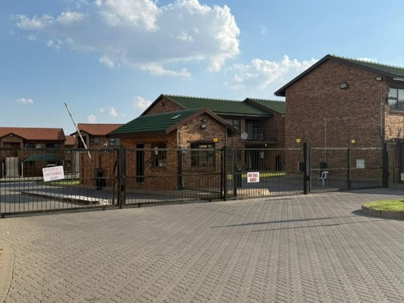The entrance to the apartment complex features a secure gated access point with a guard house, paved driveway, and perimeter electric fencing.