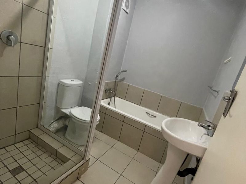 A functional bathroom featuring a pedestal basin, built-in bathtub, and a separate shower enclosure with tiled finishes throughout.