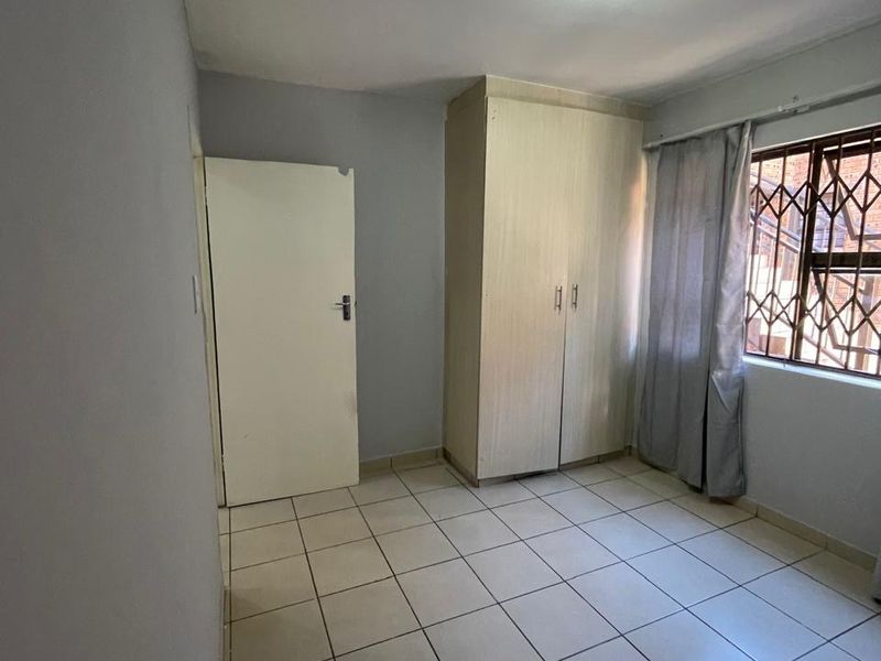 A clean, empty bedroom featuring neutral tiled flooring, a built-in wardrobe, and a window fitted with a security gate.