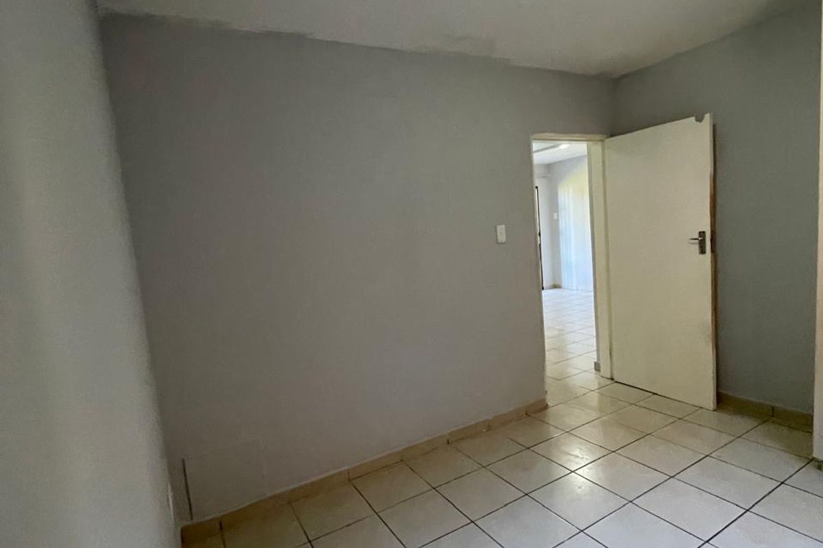 An empty bedroom featuring neutral grey walls, tiled flooring, and a standard ceiling light fixture, providing a blank canvas for interior design.