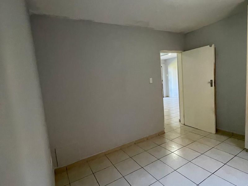 An empty bedroom featuring neutral grey walls, tiled flooring, and a standard ceiling light fixture, providing a blank canvas for interior design.