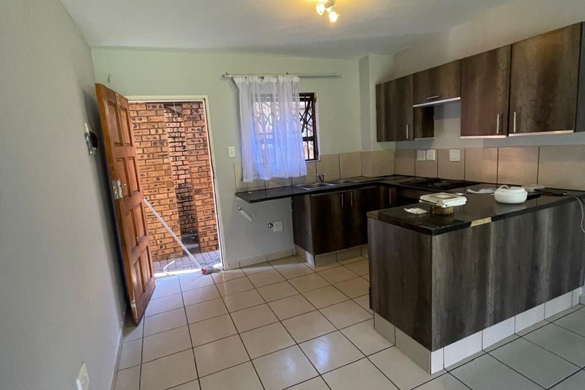 Open-plan kitchen featuring dark wood-look cabinetry, laminate countertops, tiled flooring, and direct access to an exterior area through a security door.
