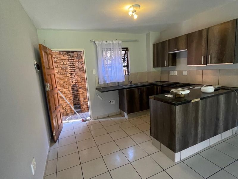 Open-plan kitchen featuring dark wood-look cabinetry, laminate countertops, tiled flooring, and direct access to an exterior area through a security door.