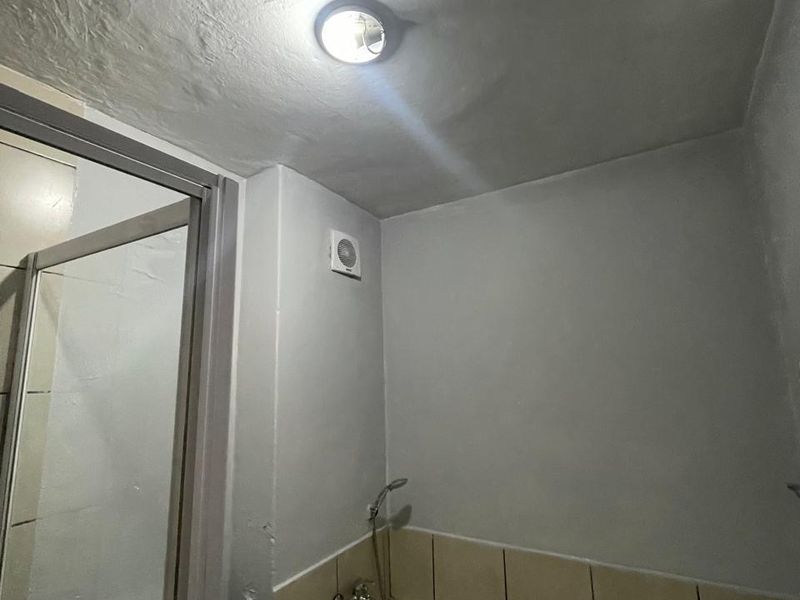 A compact bathroom featuring a bathtub with a shower mixer, a toilet, and an integrated extractor fan.