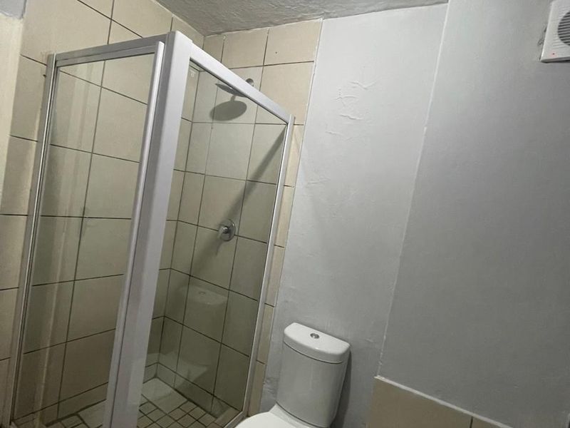A functional bathroom featuring a shower enclosure, toilet, and bathtub with tiled finishes, requiring some cosmetic updates to the wall surfaces and grout.