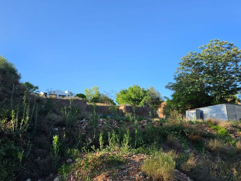 A view of the rear section of the vacant residential land, featuring a retaining wall, corrugated metal shed, and natural vegetation.