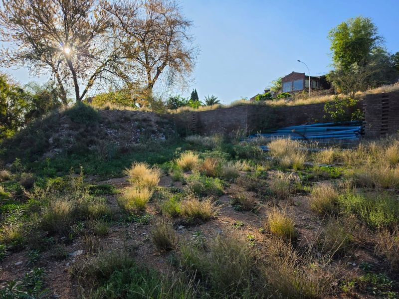 A view of the rear section of the vacant residential land, featuring a brick retaining wall and natural sloped terrain.