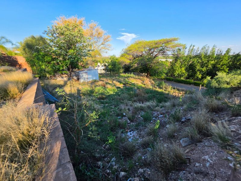 A sloped residential plot featuring a retaining wall, mature trees, and a small metal storage shed on the property.