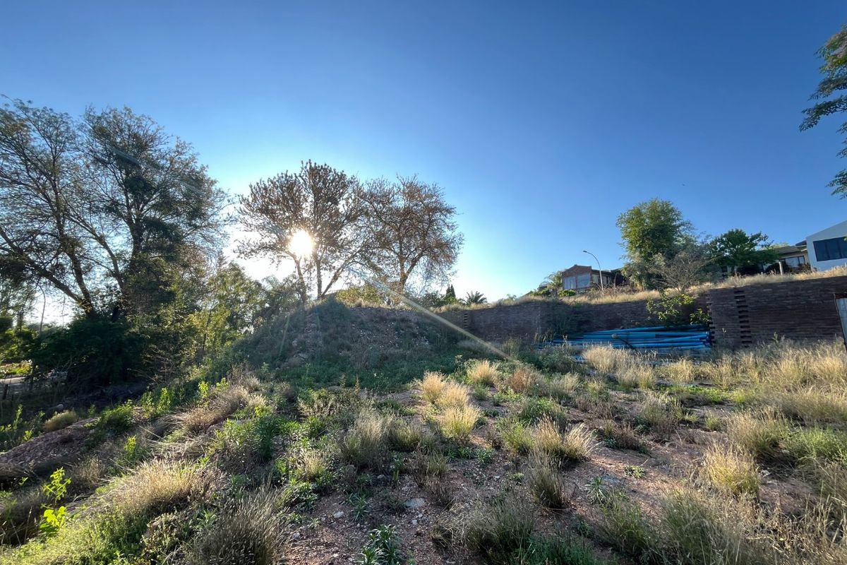A view of the sloped residential land featuring a brick retaining wall and natural vegetation under a clear sky.