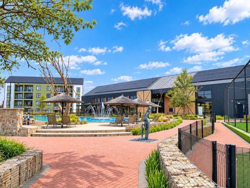 Well-maintained communal pool area featuring a water fountain, paved pathways, and modern apartment buildings with integrated solar panels.