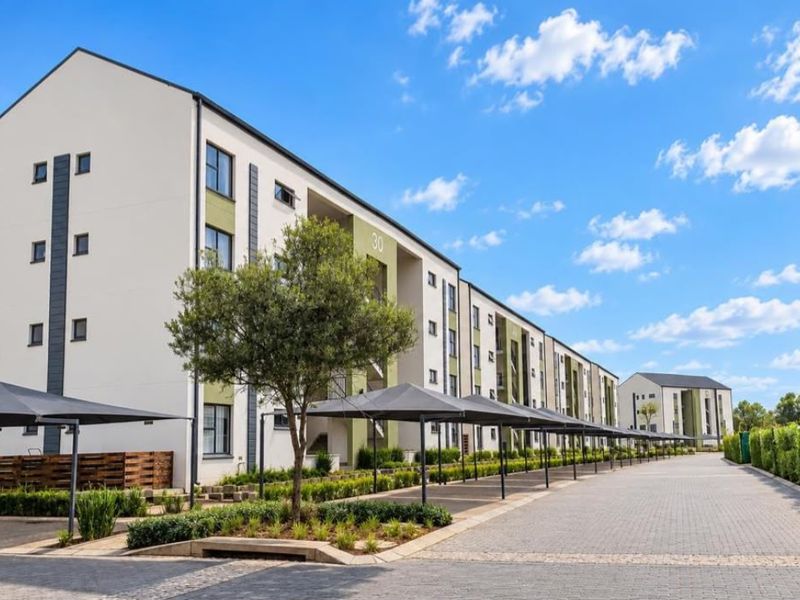 A well-maintained multi-story apartment complex featuring paved driveways, covered parking bays, and neat landscaped garden areas.