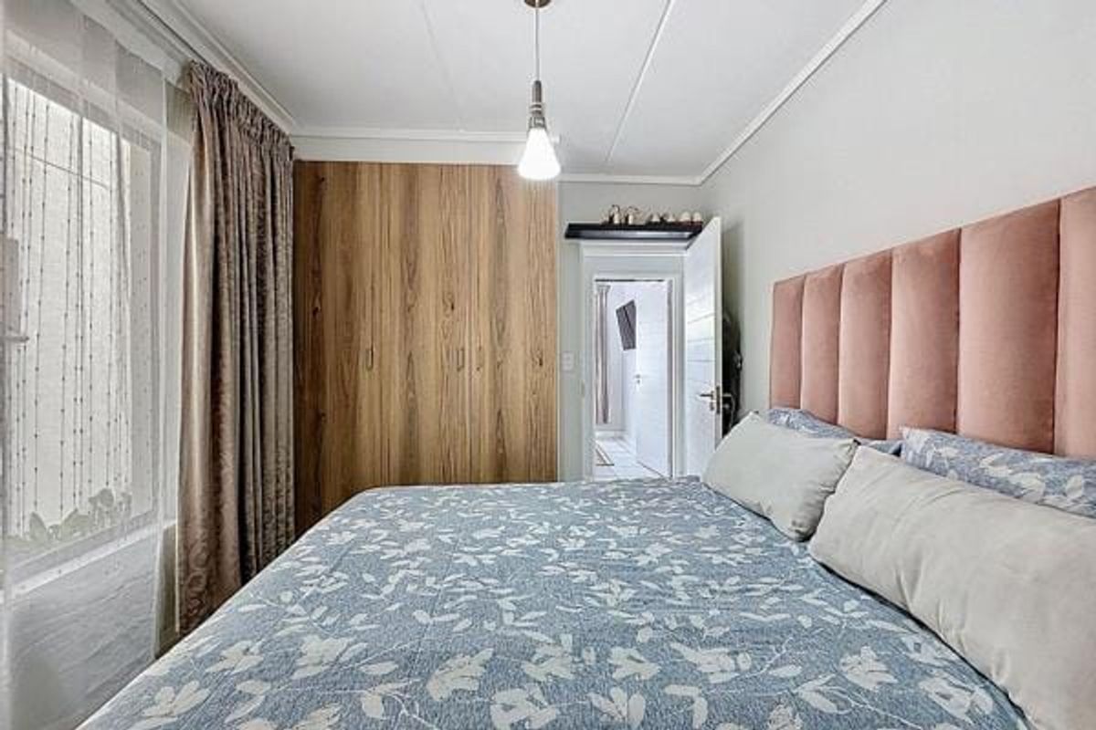 A well-maintained bedroom featuring a large built-in wooden wardrobe, coved ceiling, and a pendant light fixture.