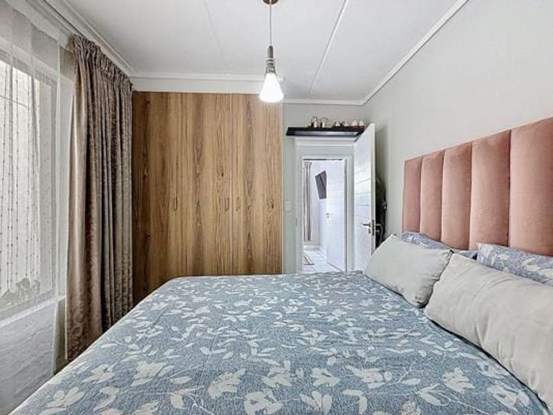 A well-maintained bedroom featuring a large built-in wooden wardrobe, coved ceiling, and a pendant light fixture.