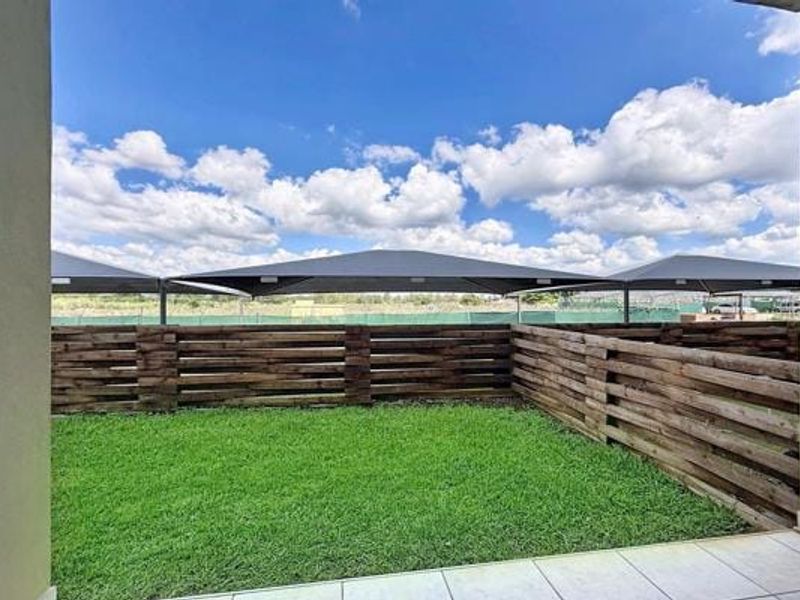 A private rear garden area featuring a tiled patio, timber slat fencing, and overhead shade sails, offering a clean and well-maintained outdoor space.