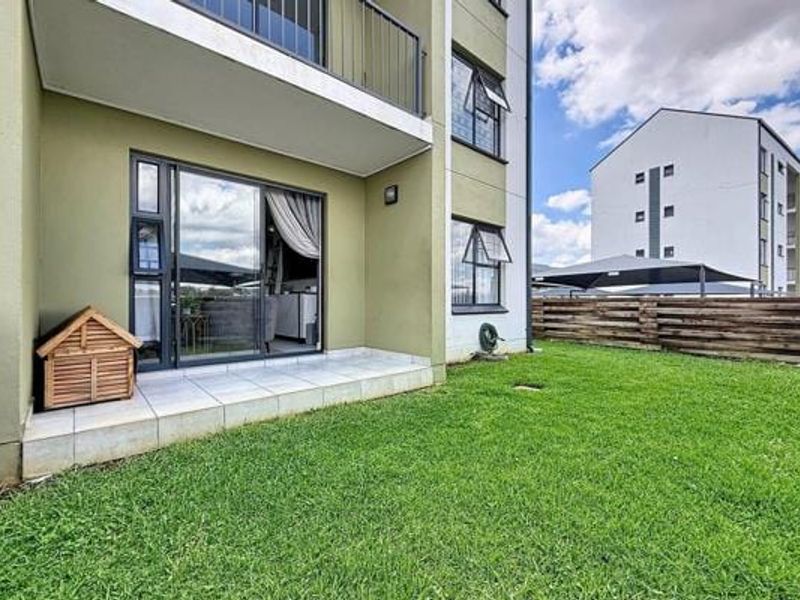 A ground floor apartment featuring a private tiled patio area leading onto a small, well-maintained lawn with timber fencing.