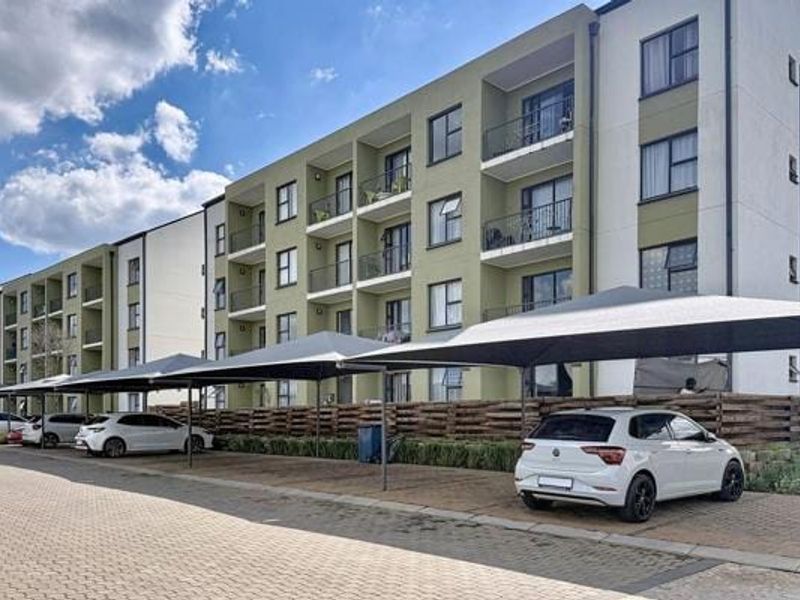 Exterior view of a modern apartment complex featuring multi-level balconies and dedicated shade cloth parking bays for residents.