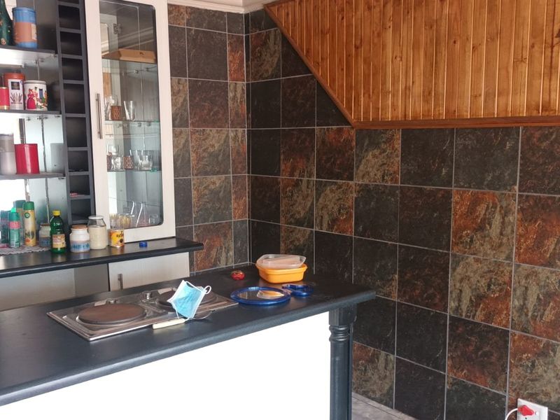 A kitchen area featuring stone-look wall tiling, timber ceiling paneling, built-in cabinetry with glass display sections, and a fitted electric cooktop.