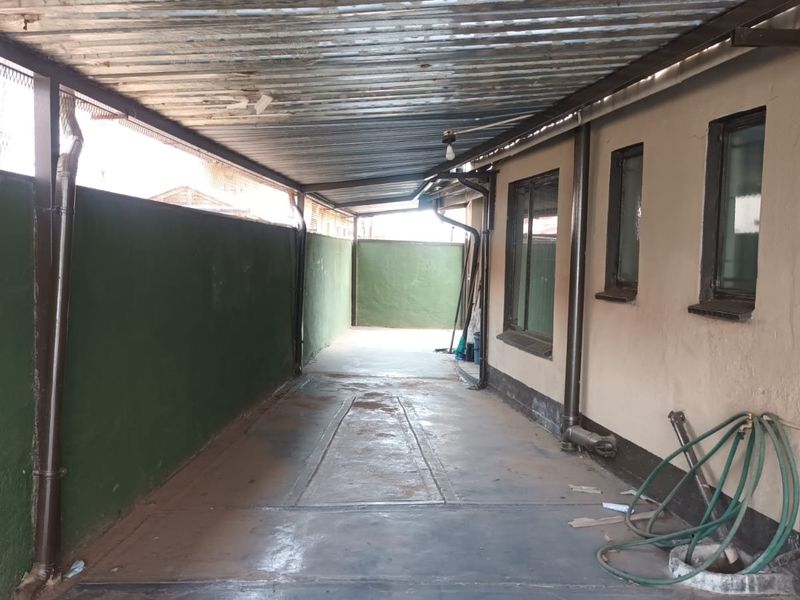 A covered outdoor parking area or garage space featuring a corrugated metal roof, concrete flooring, and perimeter boundary walls.