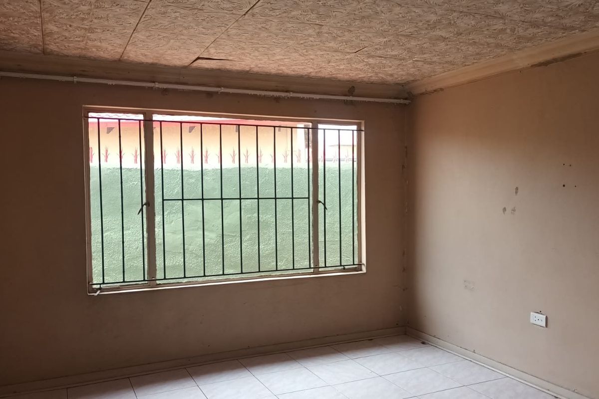 An empty living room featuring tiled flooring, textured ceiling tiles, and a large window fitted with security bars.
