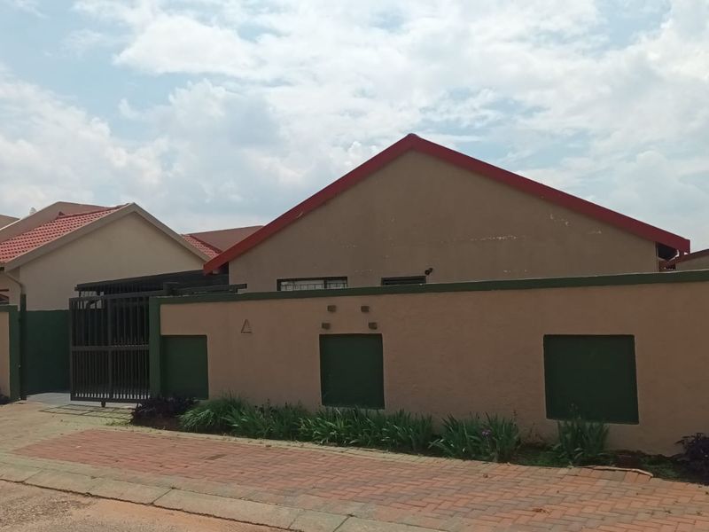 Front exterior view of a residential house featuring a perimeter wall, metal driveway gate, and paved verge area.
