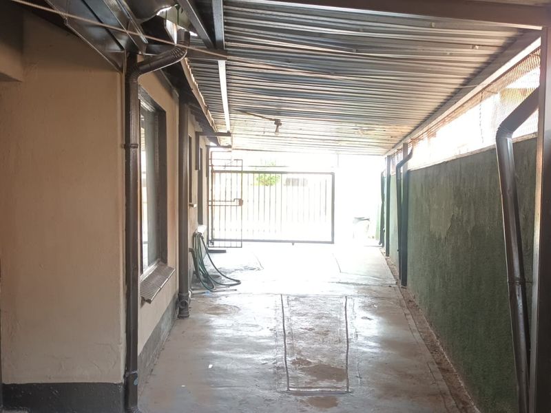 A covered driveway or carport area featuring a corrugated metal roof, concrete flooring, and secure gated access.