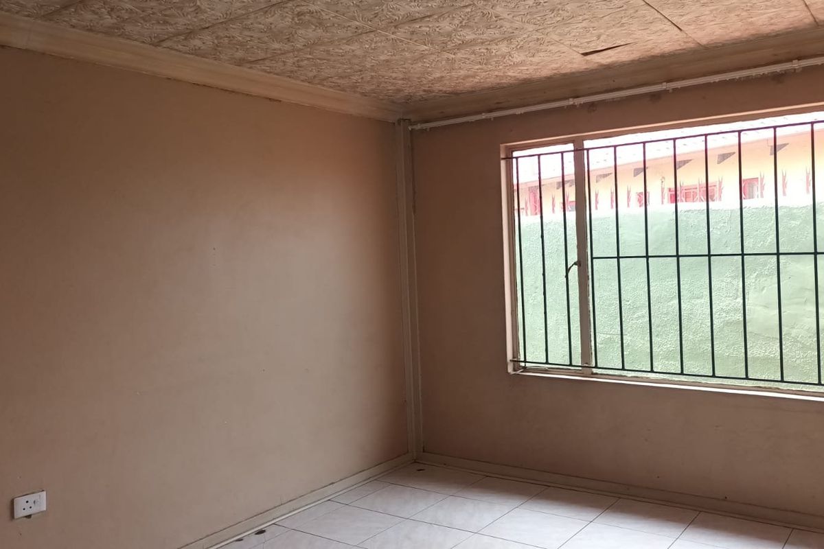 An empty bedroom featuring tiled flooring, security bars on the window, and textured ceiling tiles in need of repair.