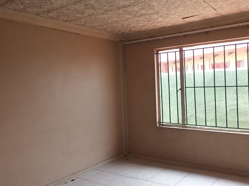 An empty bedroom featuring tiled flooring, security bars on the window, and textured ceiling tiles in need of repair.