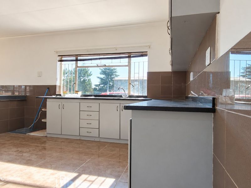 A functional kitchen featuring tiled flooring, built-in cabinetry, laminate countertops, and a tiled backsplash with a window overlooking the exterior.
