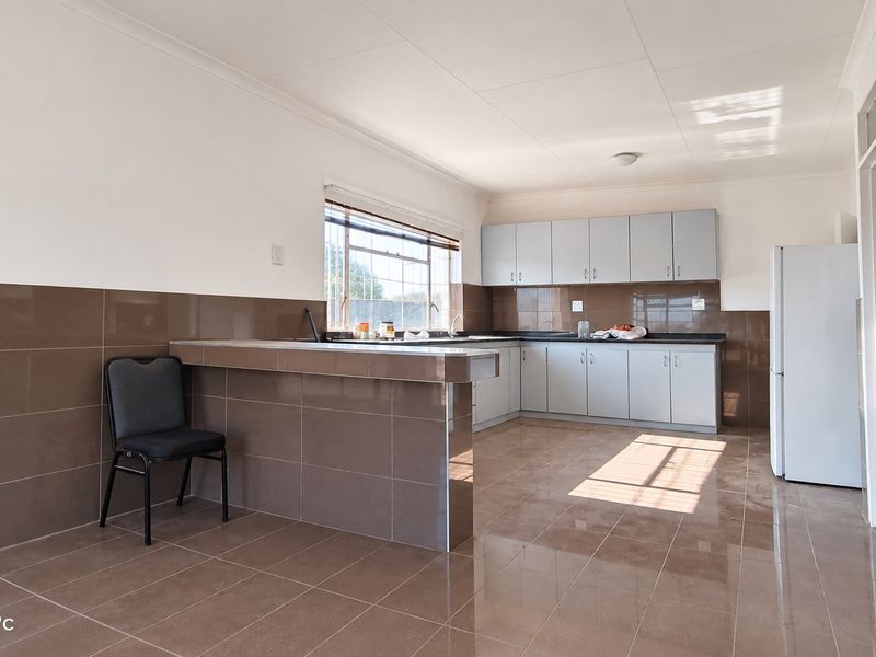 A spacious kitchen featuring tiled flooring, extensive wall tiling, built-in cabinetry, and a breakfast counter, offering a functional layout for meal preparation.