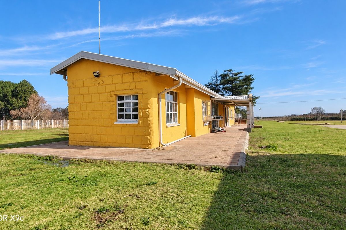 Rear view of a yellow painted brick farmhouse featuring a paved patio area and surrounding lawn.