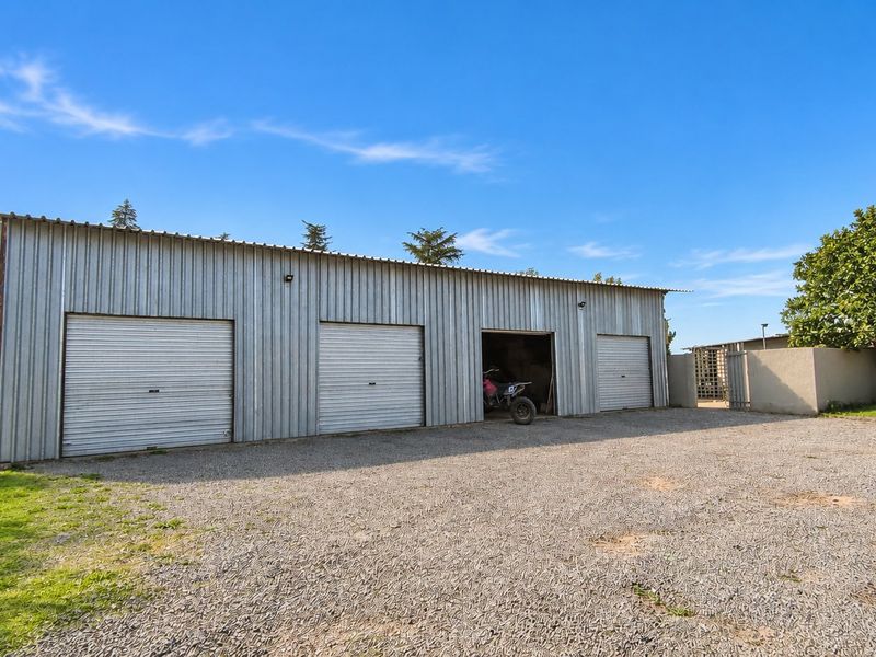 A large, functional triple-bay garage featuring corrugated metal construction and roller shutter doors, situated on a gravel driveway.