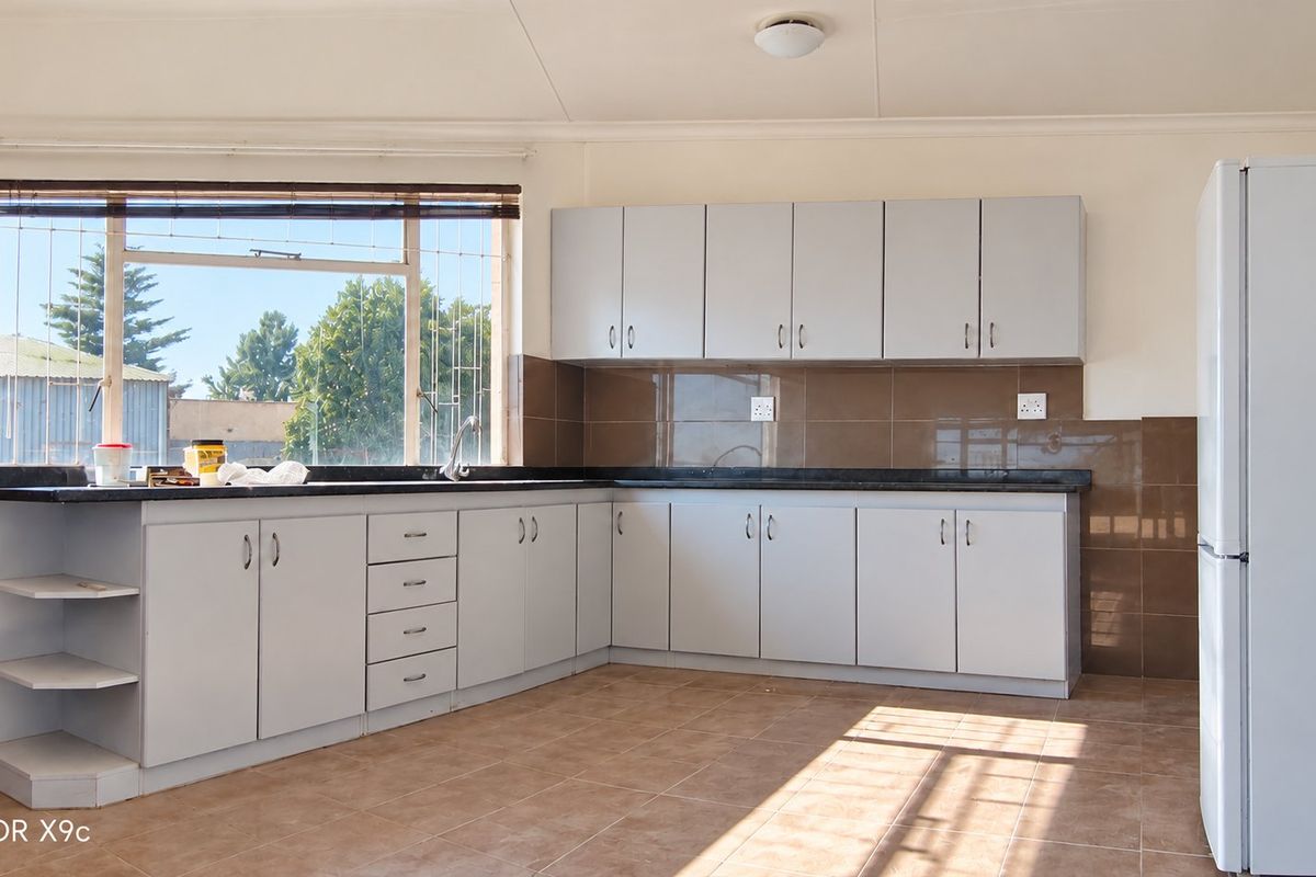 A functional kitchen featuring light-colored built-in cabinetry, dark tiled backsplash, tiled flooring, and ample counter space with a window view.