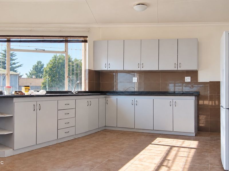 A functional kitchen featuring light-colored built-in cabinetry, dark tiled backsplash, tiled flooring, and ample counter space with a window view.