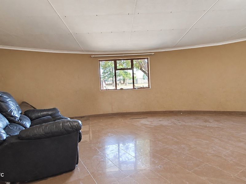 Spacious living area featuring tiled flooring, a curved wall design, and an aluminium-framed window, offering a blank canvas for interior updates.