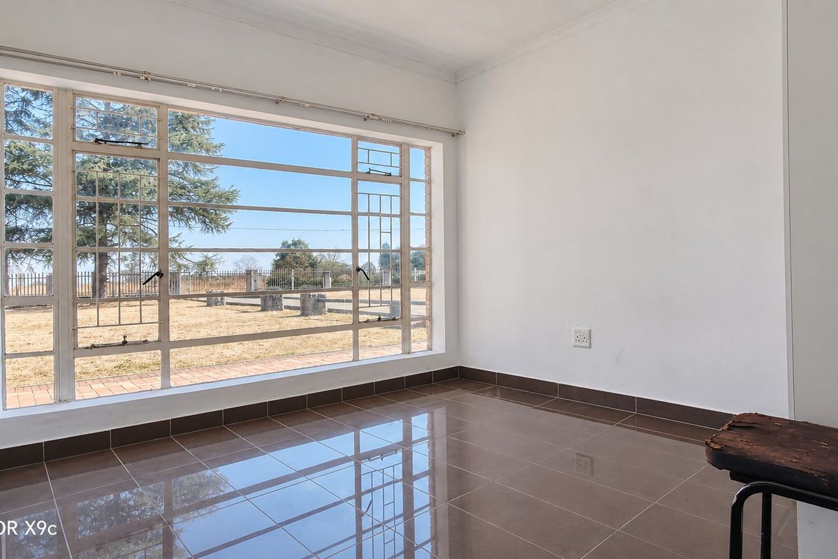 A bright, empty living area featuring large steel-framed windows that provide ample natural light and views of the surrounding farm grounds.