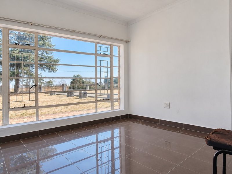A bright, empty living area featuring large steel-framed windows that provide ample natural light and views of the surrounding farm grounds.