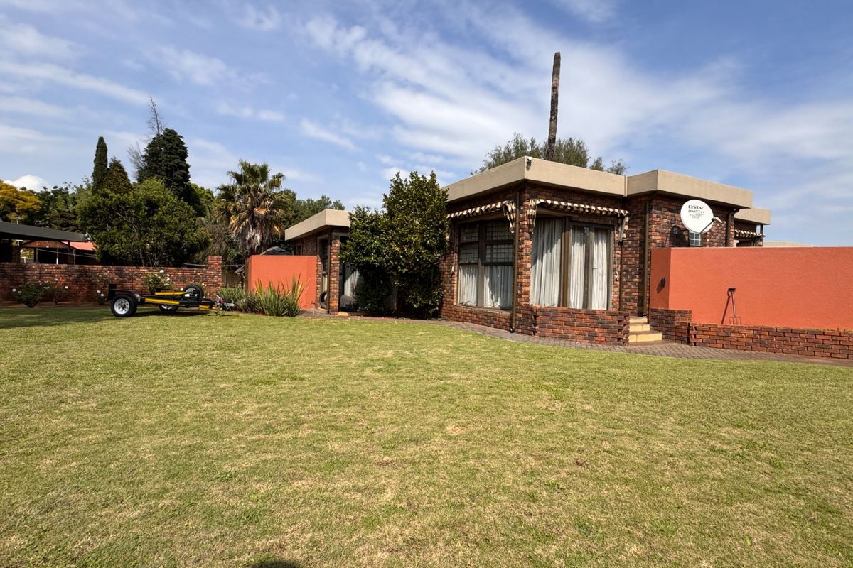 A view of the rear exterior featuring a face brick facade, flat roof design, and a spacious lawn area with a paved walkway.