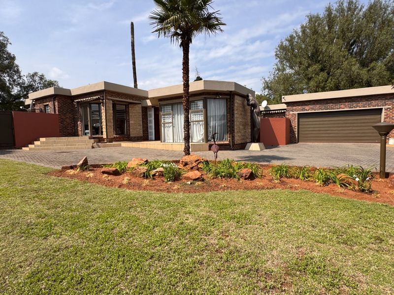 Front view of a single-story brick house featuring a paved driveway, double garage, and a well-maintained landscaped garden.