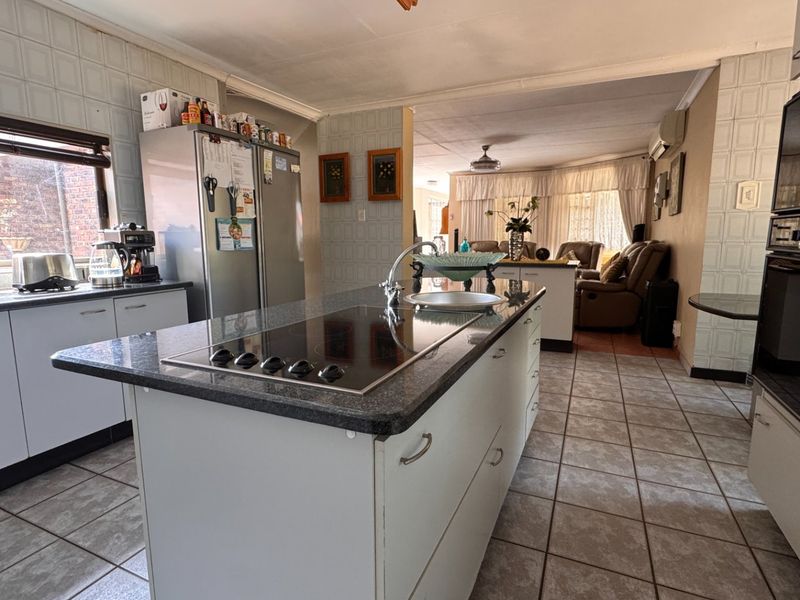 Open-plan kitchen featuring a central island with an integrated cooktop, built-in oven, and tiled flooring, flowing into the adjacent living area.