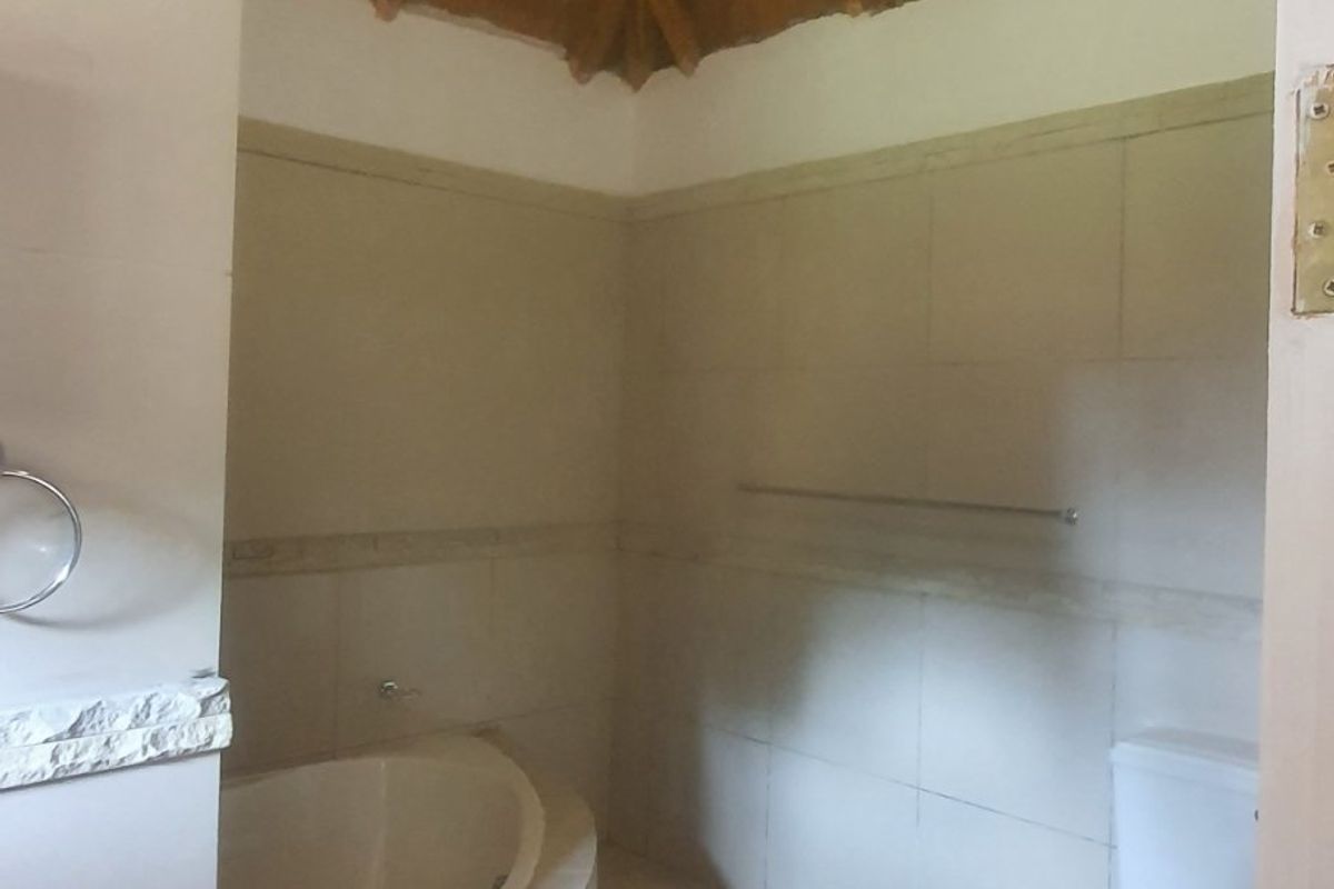 A bathroom featuring a built-in bathtub, toilet, and unique high-pitched thatched roof with exposed timber rafters.