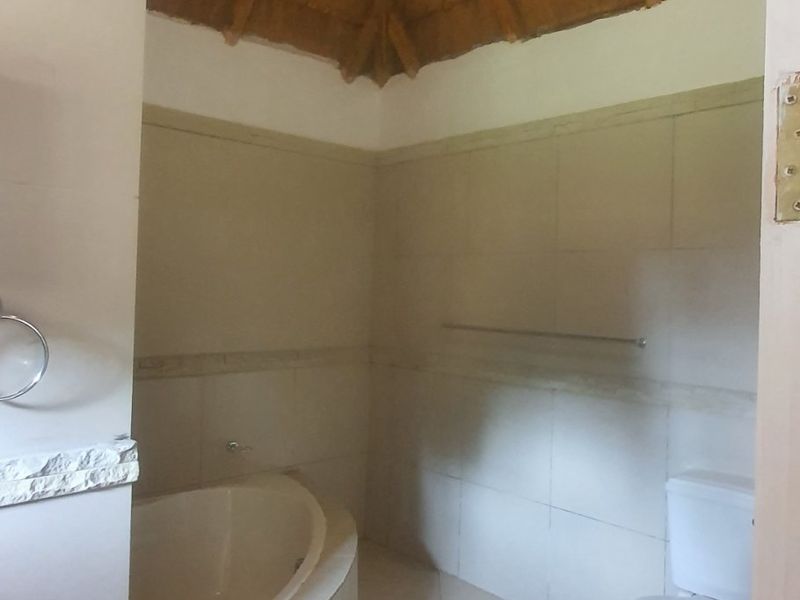 A bathroom featuring a built-in bathtub, toilet, and unique high-pitched thatched roof with exposed timber rafters.