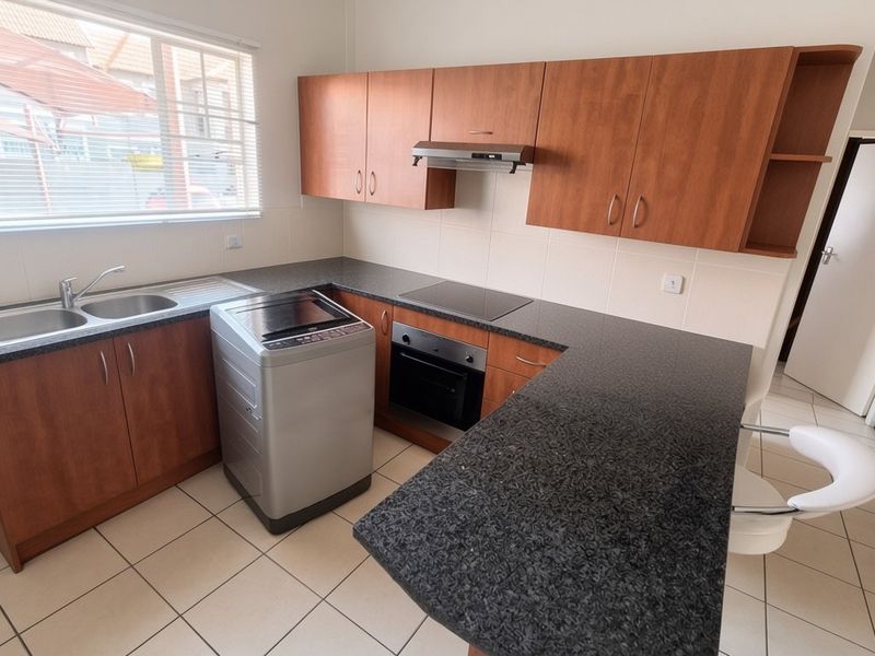 Functional kitchen featuring laminate cabinetry, granite countertops, built-in oven, electric hob, extractor fan, and tiled flooring with a breakfast nook area.