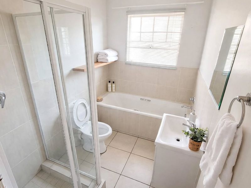 A clean, functional bathroom featuring a separate shower enclosure, bathtub, vanity basin, and neutral wall and floor tiling.
