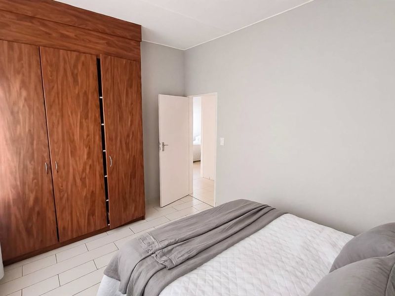A well-maintained bedroom featuring built-in wooden wardrobes and neutral tiled flooring, offering a clean and functional living space.