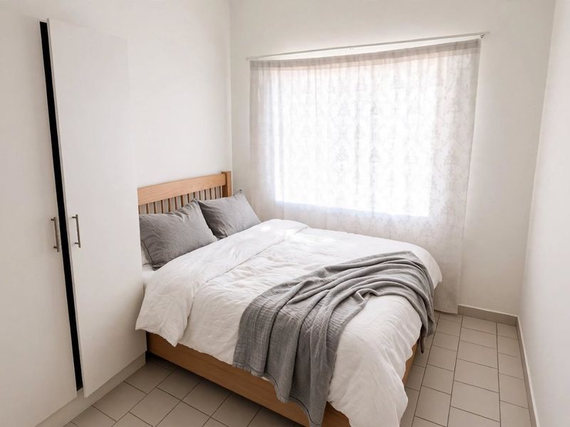 A compact bedroom featuring neutral tiled flooring and a built-in wardrobe, offering a clean and functional living space.